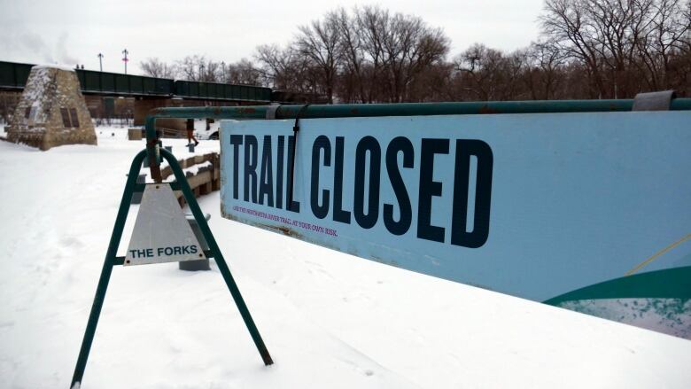 A barricade blocks access to a river skating trail. A sign reads: Trail closed.