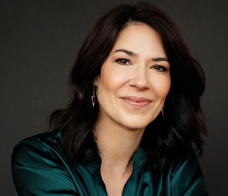 A head and shoulders portrait of a smiling woman with dark hair who's wearing a shiny green blouse.