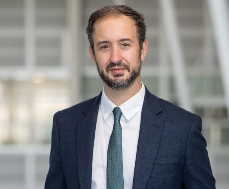 An upper body portrait of a bearded man wearing a suit jacket and tie.