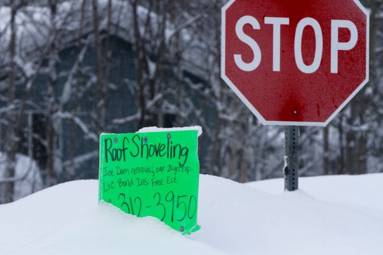 A handmade sign sits in the snow beside a stop sign.