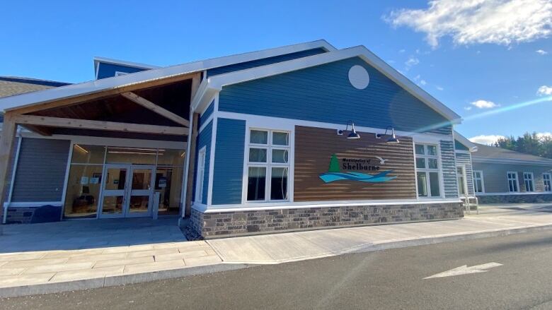 A blue one-story building is seen with a brown section at the front of the building with the municipality's logo