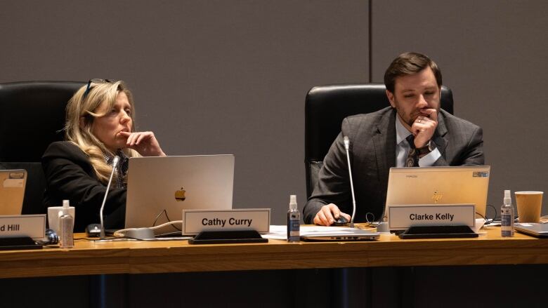 A woman leans back in her chair and listens intently while a man checks his computer