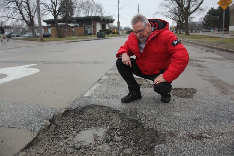 A man wearing a red jacket looking at a pothole in a road