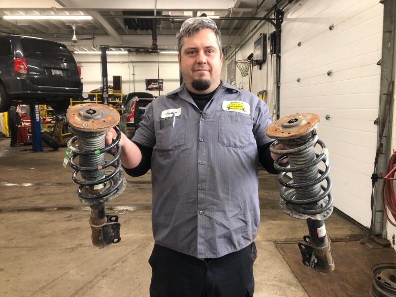 A car mechanic holding two damaged parts of a car's suspension