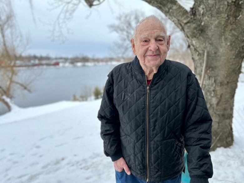 A man in a black jacket stands outside on a snowy day.