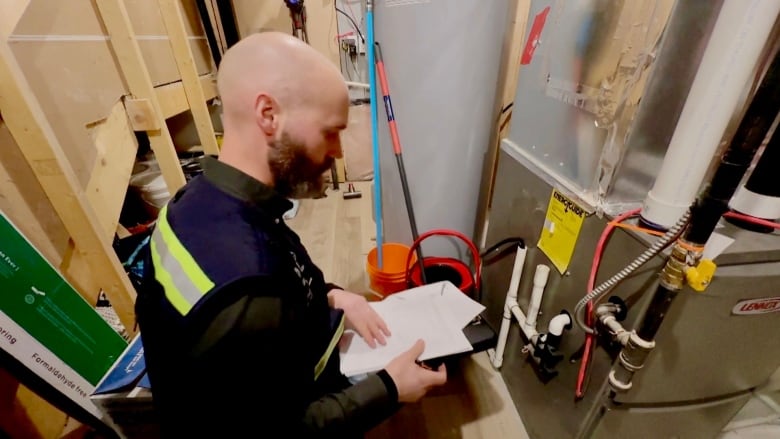 An energy assessor looks at a furnace and writes down information on a piece of paper.