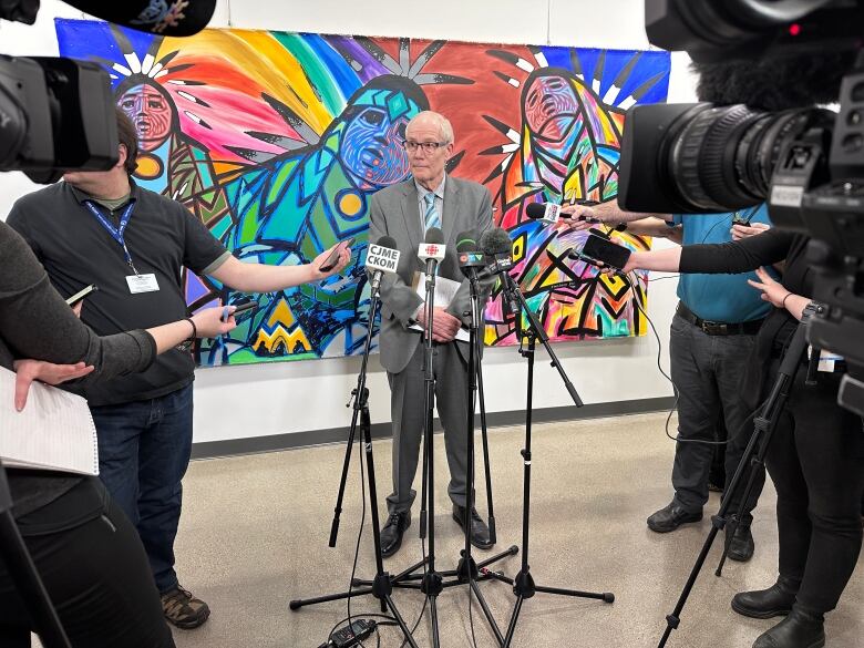 A man with grey hair and glasses speaks at a news conference.