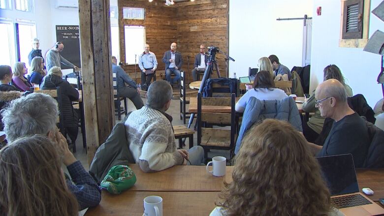 People at tables watch the three candidates debate in a corner of the room.