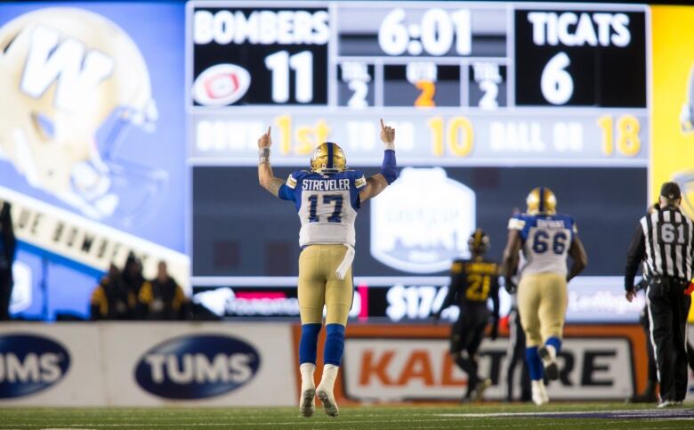 A football player holds his hands up in celebration while facing a giant scoreboard