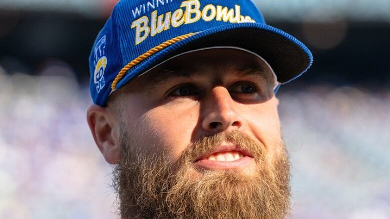 A man with a bushy beard and a blue baseball cap smiles and looks off to the side of the photo frame