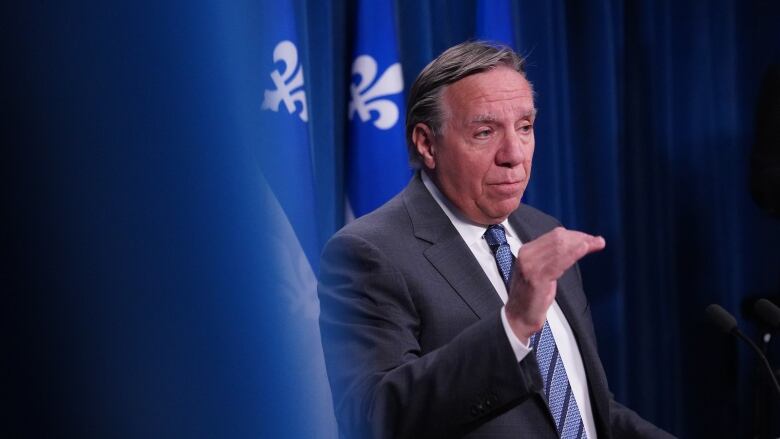 Premier Legault speaks to media in front of blue background.