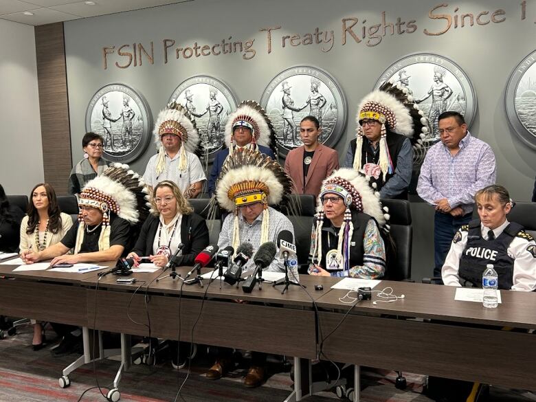 Several people, including in headdresses, sit and stand at a table