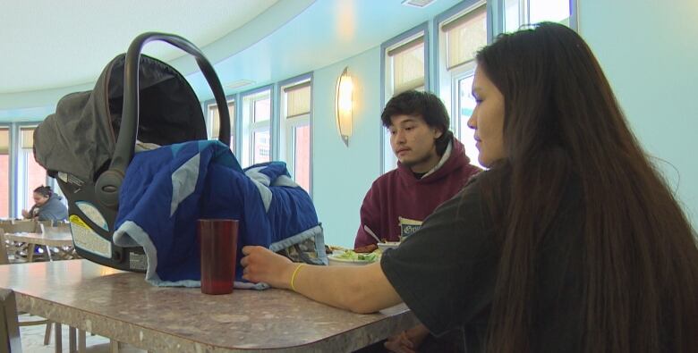 A young First Nations couple sit at a lunch table with a baby in a bassinet.