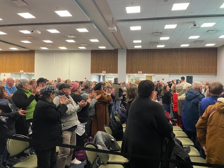 A crowd of people stands and claps in a conference room