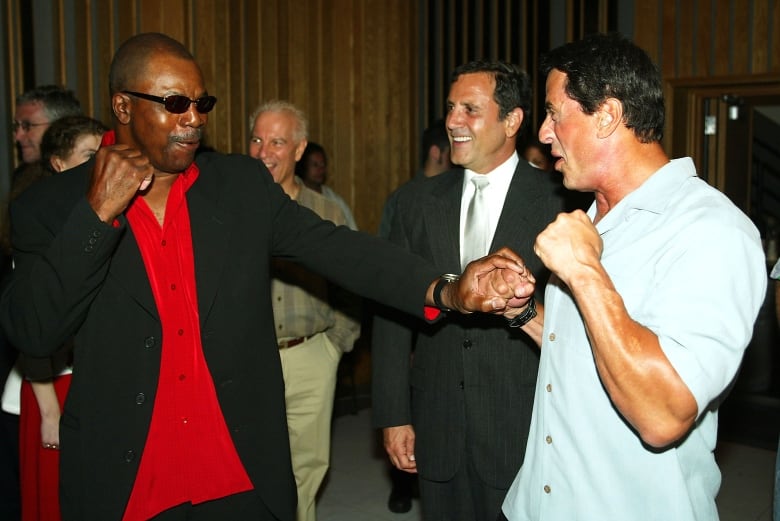 Two smiling men jokingly hold their fists up as if about to fight. 