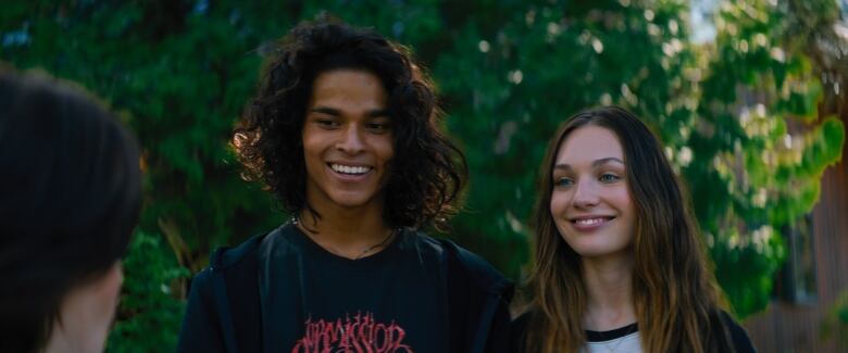 A smiling teen boy and girl stand in front of a blurred green background. 