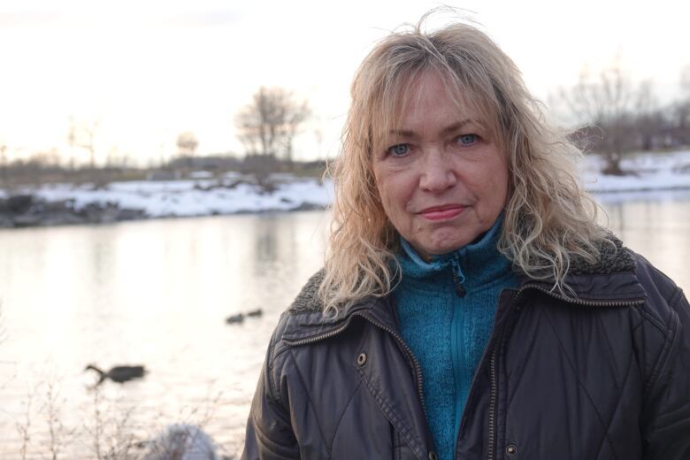 A headshot of a blonde woman on a rocky beach.