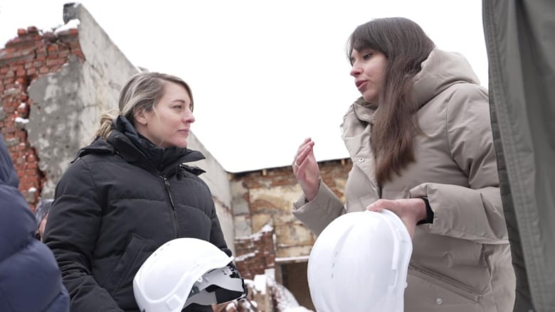 Three women talk, with snowy rubble in the background.