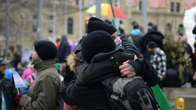 Two people hug at an outdoor protest.