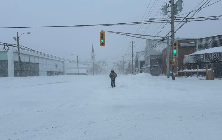 A man stands on a deserted snow-covered road with buildings on either side.