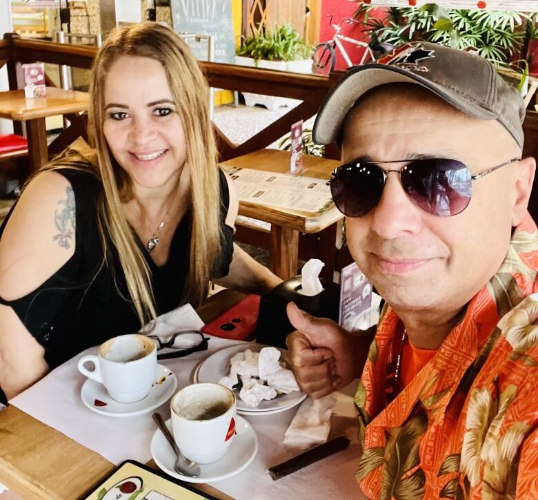 A man and a woman smile while seated at a cafe table.