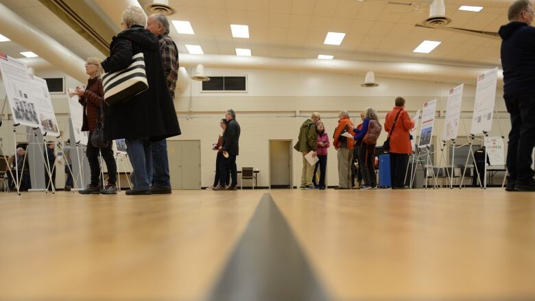 People stand in front of display boards at an open house in a community centre gym.