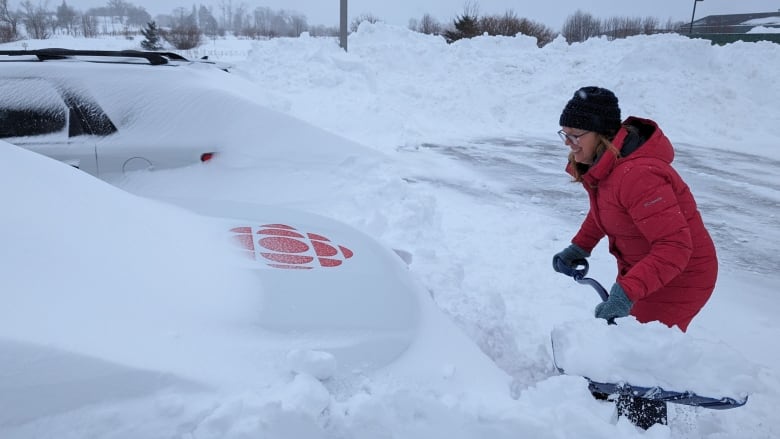 person bunlded up shovels snow from around a CBC van