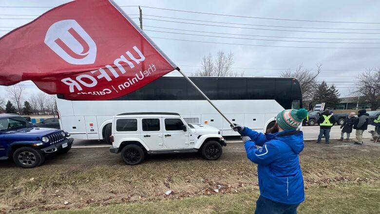 A man waves a flag in front of a white coach bus