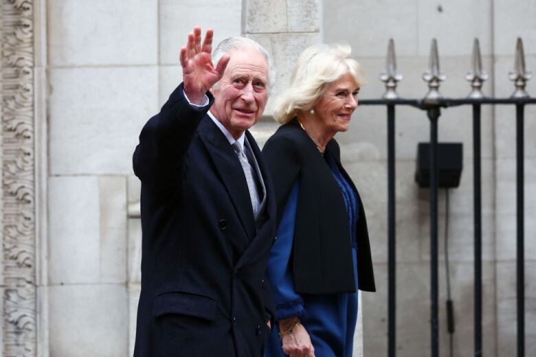 An elderly man waves as he leaves hospital hand-in-hand with his wife.