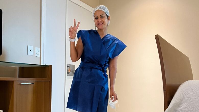 A woman in a hospital gown shows a peace sign.