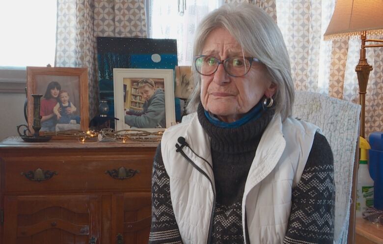 A greyhaired woman is sitting in front of framed photos of a boy.