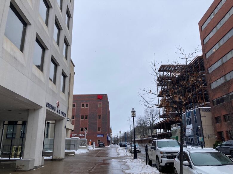 Downtown street in winter with large buildings and cars parked at meters.