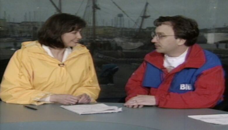 A woman in a yellow coat speaking to a man in a red and blue Labatt Blue branded coat. 