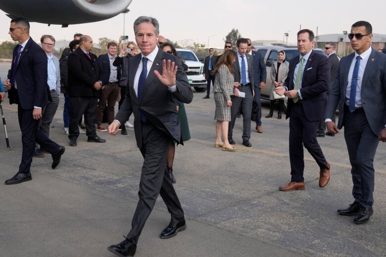 A man in a suit waves to the camera.