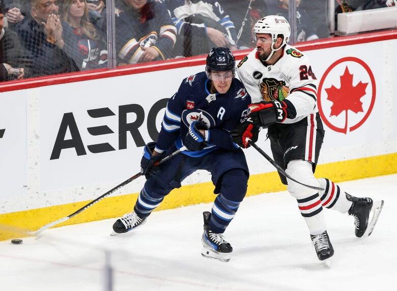 A hockey player chases another player with the beside the net.