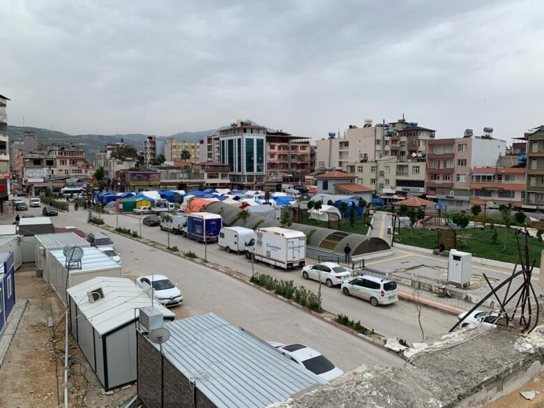 An parking lot surrounded by mobile homes and converted shipping containers and filled with blue tents. 