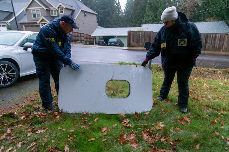 Two people with the National Transportation Safety Board hold the door plug from Alaska Airlines Flight 1282.