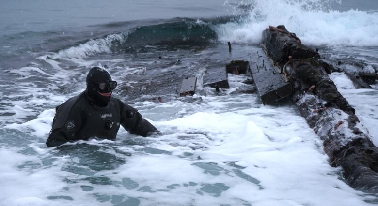 Man in wetsuit floating next to pile of wood.