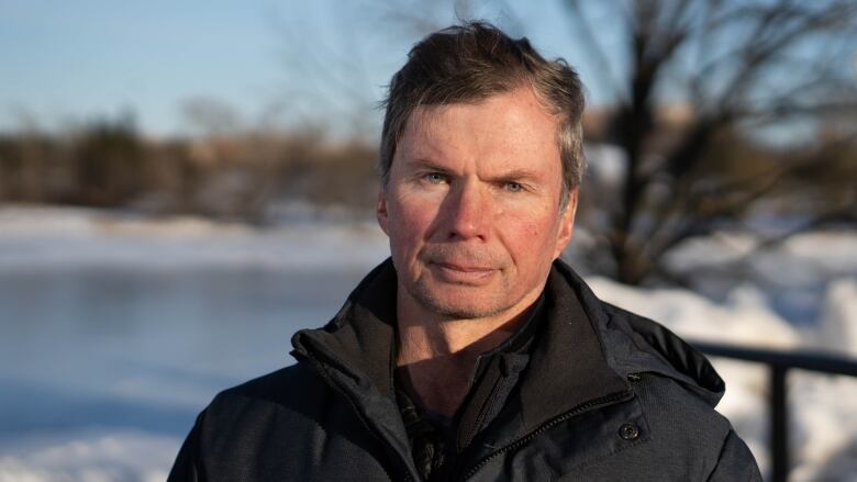 A man stands in front of a snowy body of water.