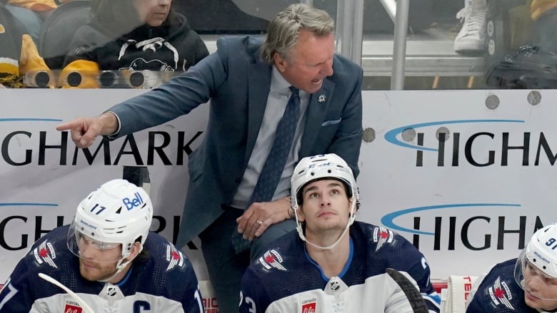 A man in a suit yells and points while standing behind three hockey players.