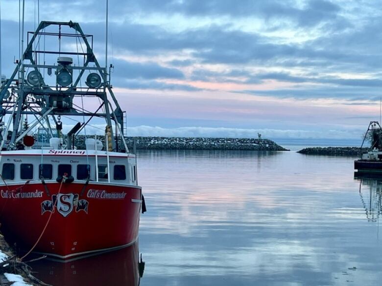 A red and white boat floats in a harbour. A pink and blue sky is reflected in the water.