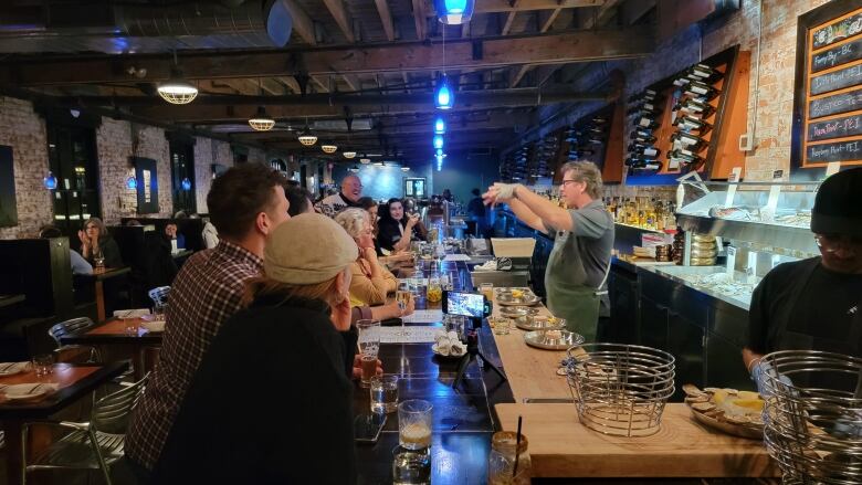 A man behind a bar talks to a group eating shucked oysters 