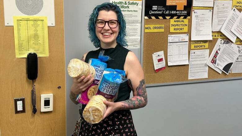 A young woman with glasses and blue hair holding rice crisps.