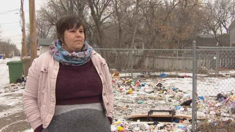 A woman stands in front of a lot covered with garbage.