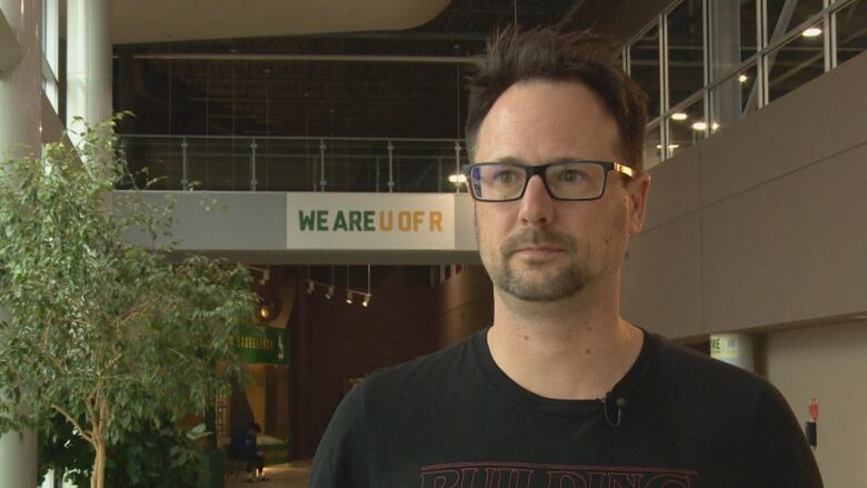 A man in glasses stands in a building.