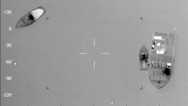 A black and white surveillance photo of three vessels in the water is shown.