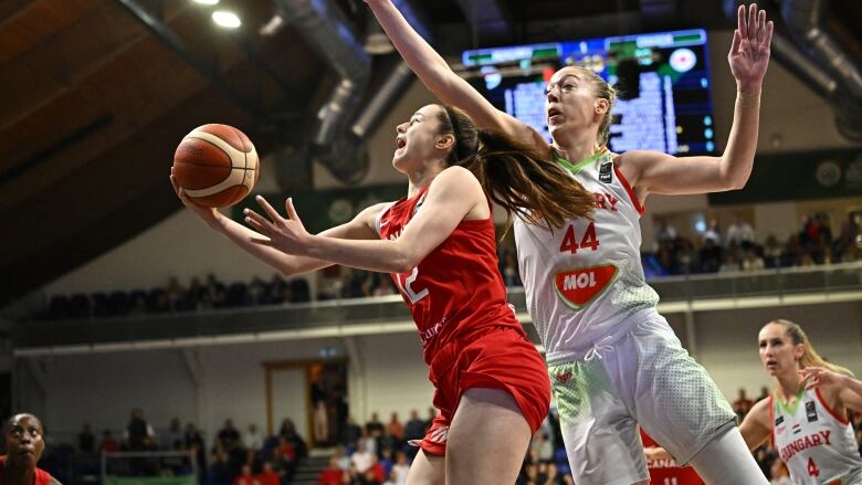 A basketball player attempts a layup as an opponent defends.