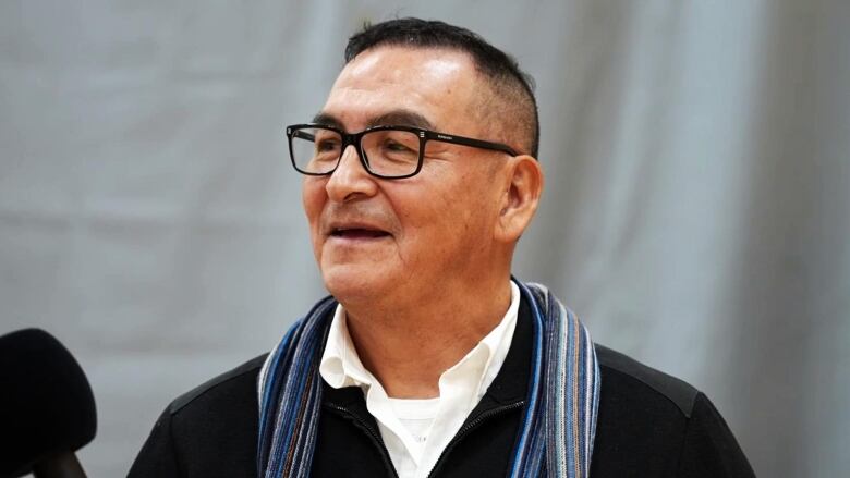 A man wearing a black sweater stands in a gymnasium. 