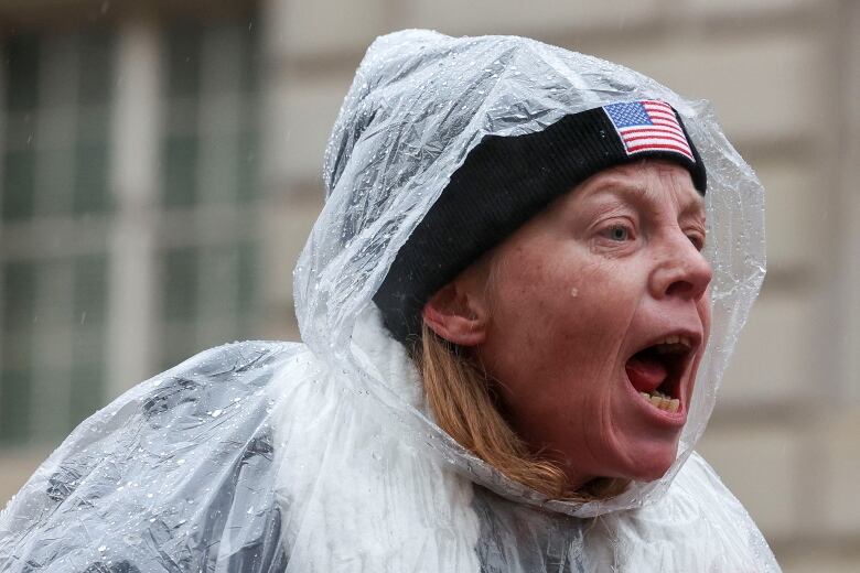 A woman shouts while wearing a rain poncho outside.