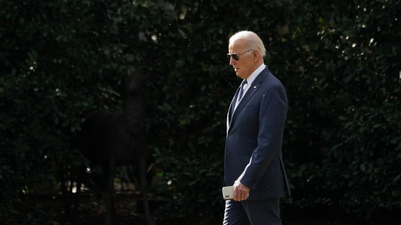 Side view of Biden walking past dark bush 